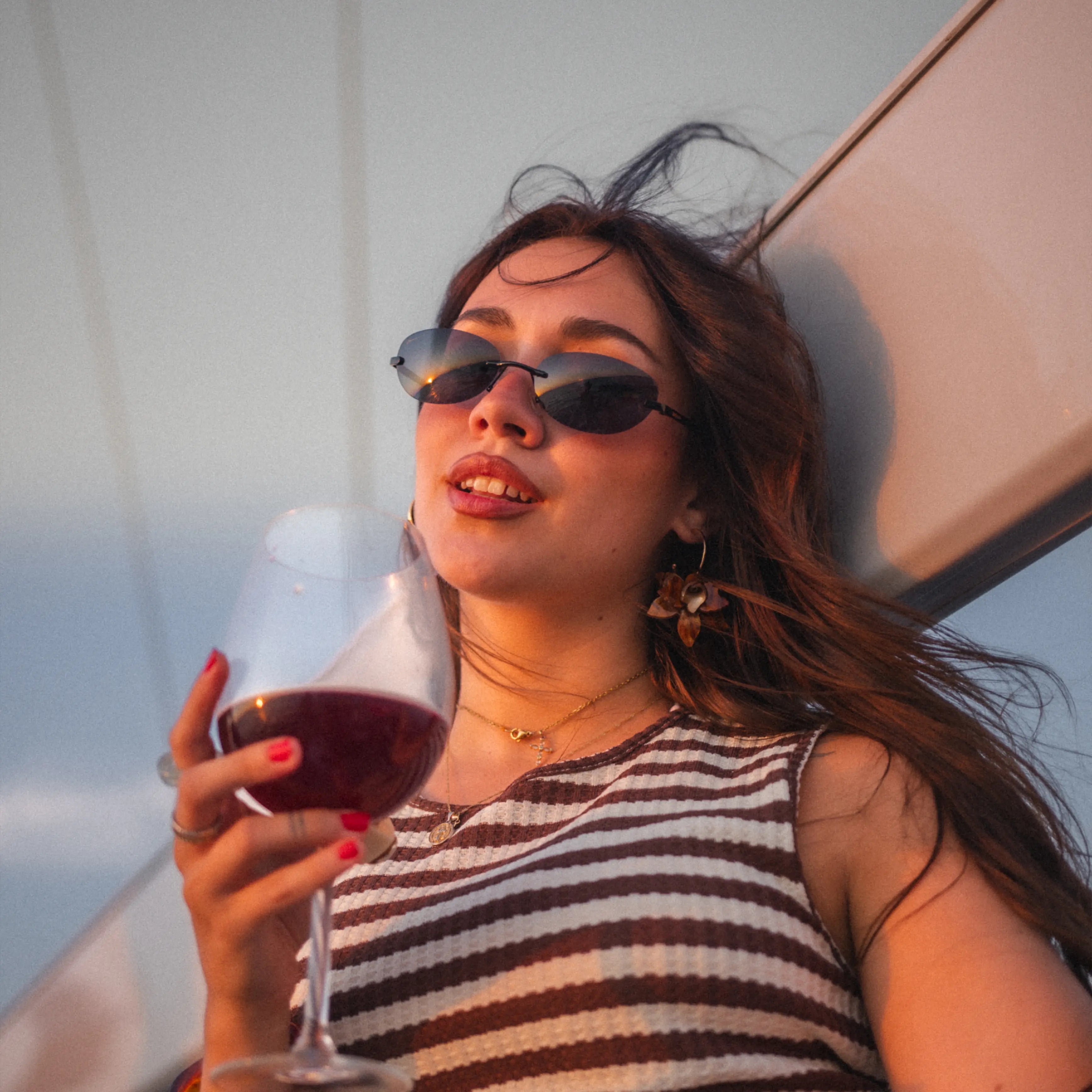 Model wearing Desire Caviar Black Sunglasses while holding a glass of wine on a boat.