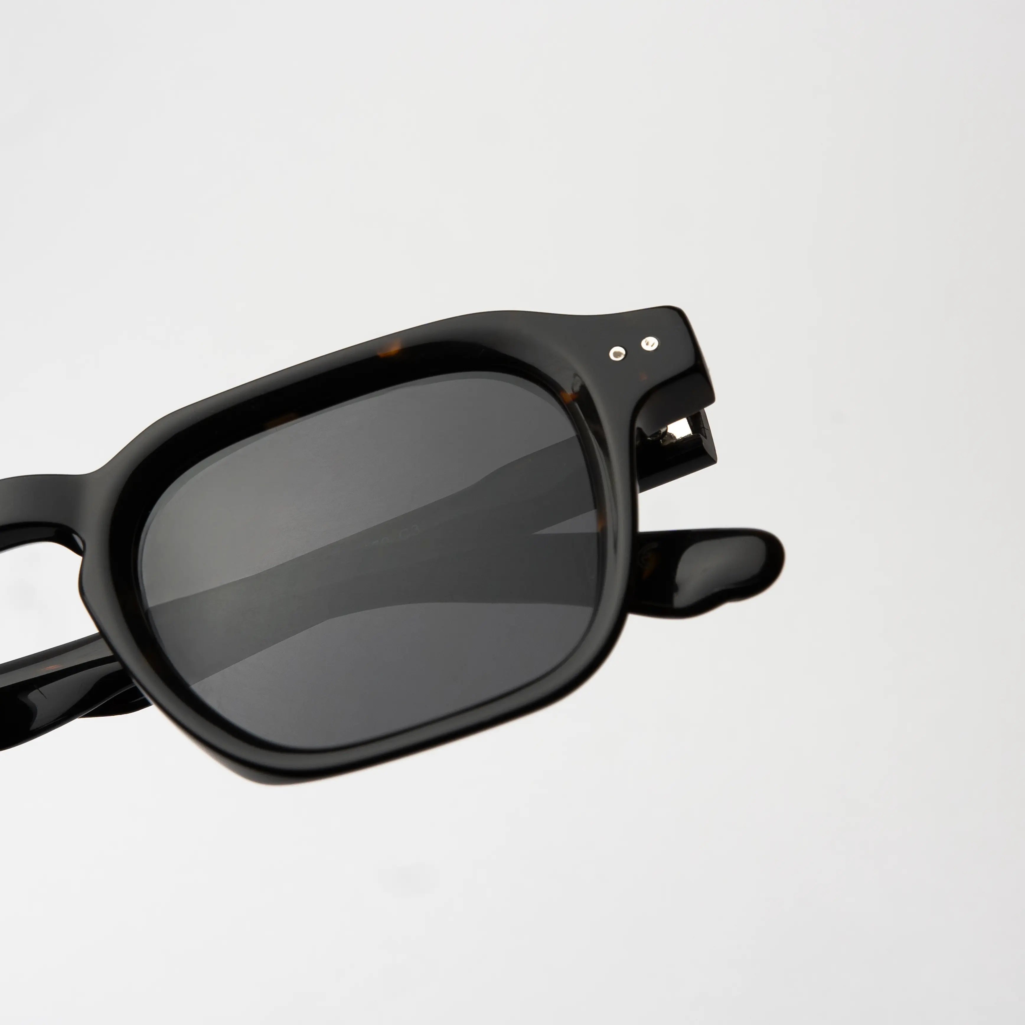 Outlaw Carey Sunglasses with a close-up of the hinge detail on the carey frame and smoke polarized lens.