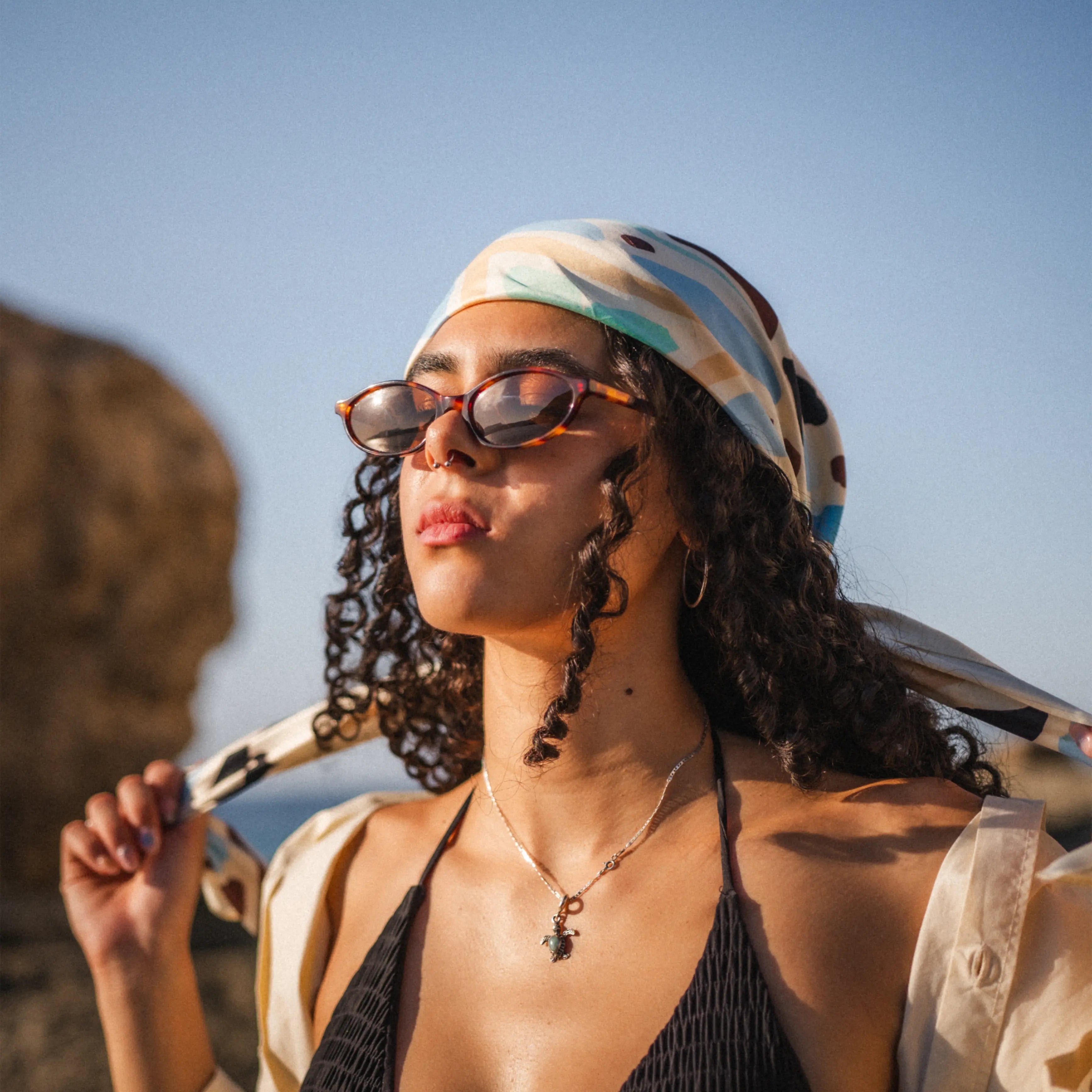 Model wearing Timeless Carey Sunglasses with a stylish scarf against a clear blue sky.